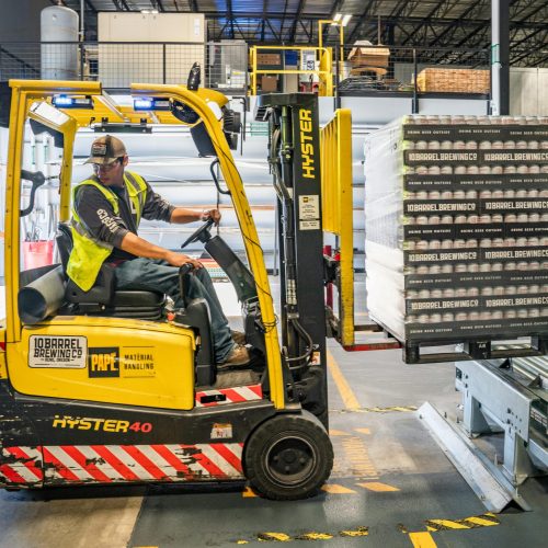pexels-photo-1267338-1267338 A warehouse worker maneuvers a forklift to transport crates for brewing company storage.